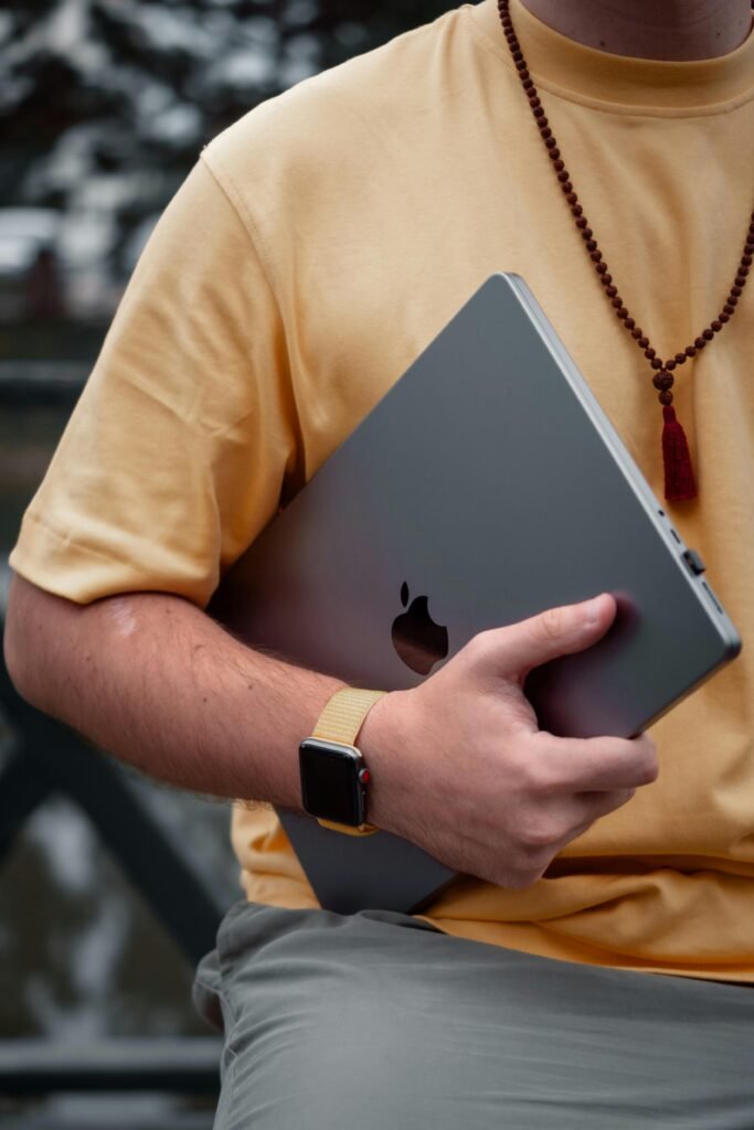 Person holding a sleek MacBook with the Apple logo, wearing a smartwatch and casual clothing, showcasing the elegance and portability of the MacBook M2